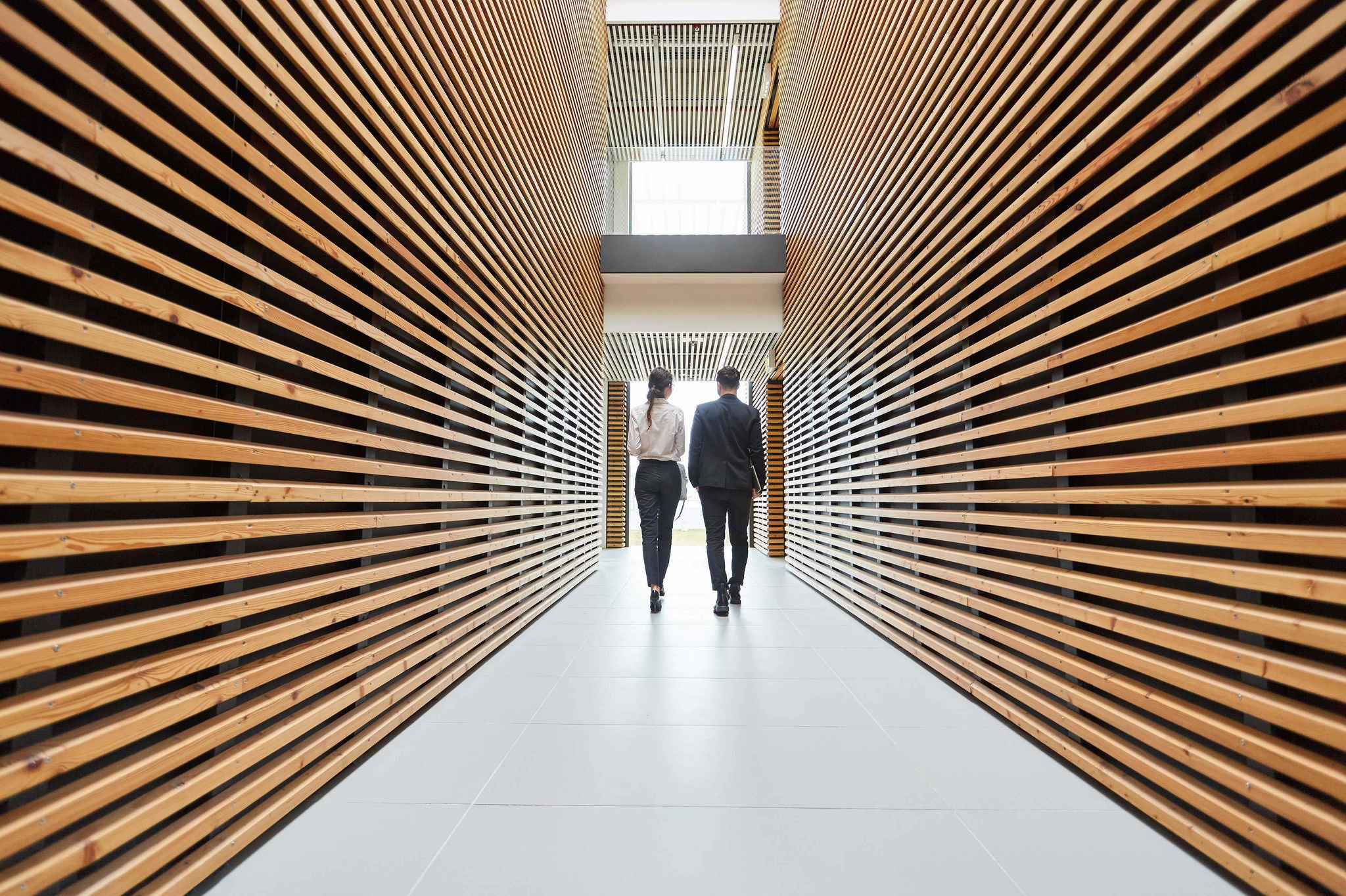 Two business people are walking in one direction in a modern office hallway